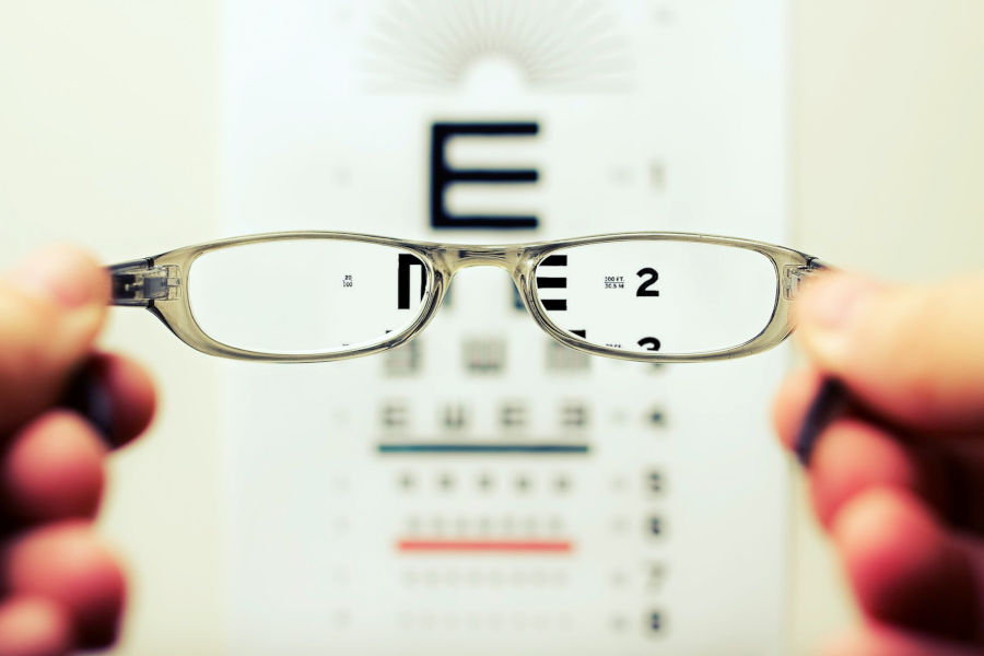 Hands holding a pair of eyeglasses up against a vision test