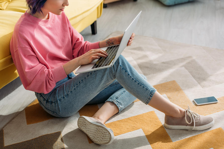 Cropped view of freelancer with colorful hair working with laptop near sofa and smartphone on floor in living room — Photo