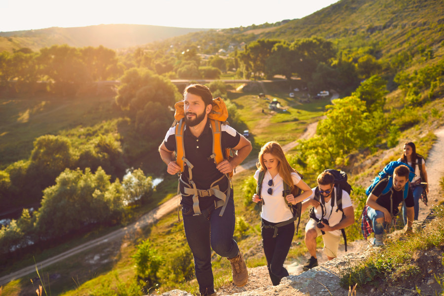 Group of young adult hikers with backpacks on their shoulders walking on the rocks in the countryside in summer weather. Concept of active recreation.